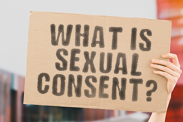 The question " What is sexual consent? " on a banner in men's hand with blurred background. Intimacy. Intimate. Sex. Adult. Law. Relationship. Love. Legality